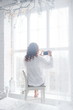 © NatBud - discount online shopping. Woman like online shopping though laptop. Curly girl in a white men's shirt sitting in a chair near the window with gadget