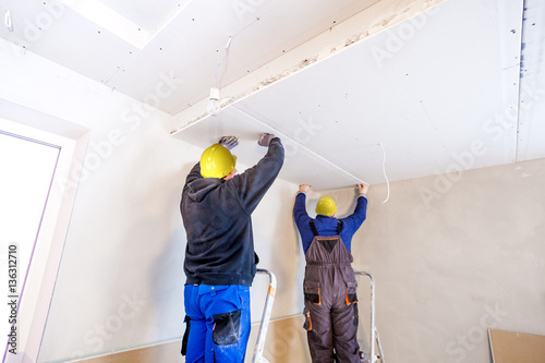 Fotografie, Tablou Workers assemble a suspended ceiling with drywall