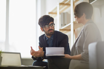 Modern middle eastern man wearing creative haircut and glasses listening intently to his colleague during  discussion of business ideas in modern office