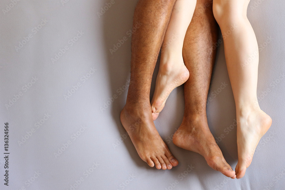 Legs of interracial couple in bed - copy space  - obrazy, fototapety, plakaty 