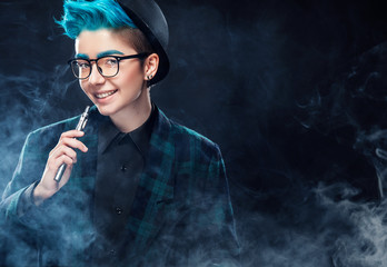 Wall Mural - smiling hipster woman with blue hair smoking vape on black background