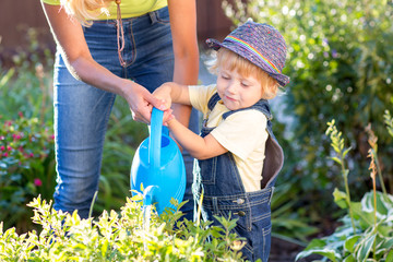 Kid with mom working in garden. Child watering flowers. Mother helps little son.