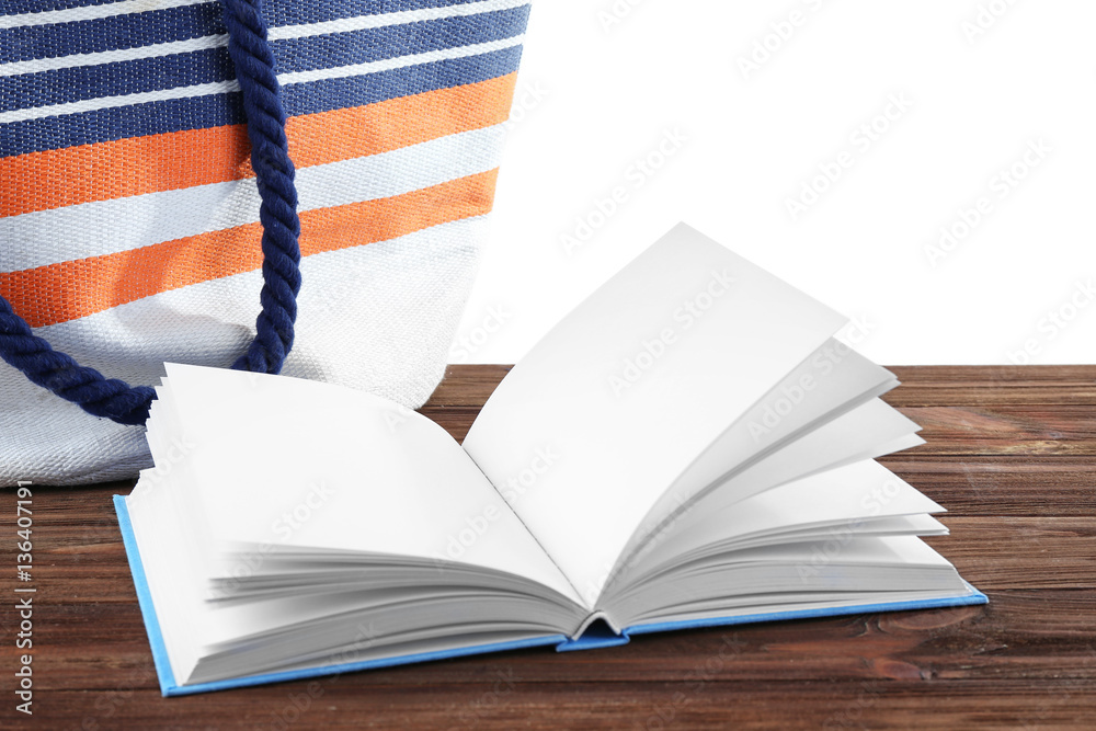 Opened book and beach bag on wooden table