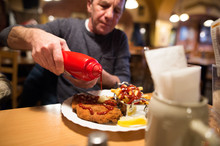 Senior Man In Restaurant Puts Ketchup On Fries And Schnitzel