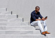 canvas print picture - young african american man sitting on steps using tablet