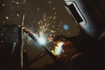 Industrial workshop man welding round pipe, colorful hot sparks