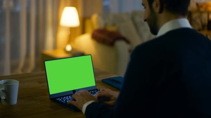 Aufkleber - At Home Back View of a  Man Sitting at His Desk and Typing on a Laptop with Green Screen on It. His Apartment is Done in Yellow colours and is Warm. Shot on RED EPIC-W 8K Helium Cinema Camera.