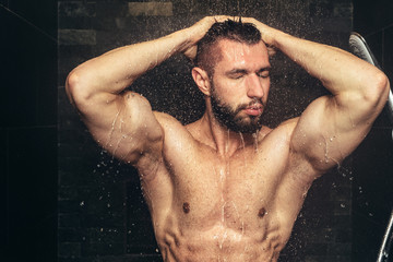 bodybuilder taking a shower after training. Handsome man in shower with water drops and splashes