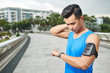 © DragonImages - Waist-up portrait of pensive Asian athlete listening to music on smartphone and checking his progress with help of fitness tracker