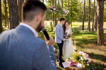 Leading or master of ceremonies, bride and groom at wedding ceremony with decorations and arch in rustic style