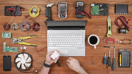 Male engineer programmer copies files from a flash card action camera on a laptop. Wooden table top view. Uses cardreader