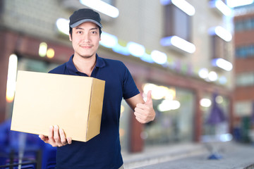 Asian Delivery man thumbs up with cardboard box on blurred backg