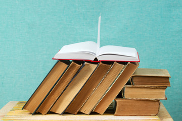 Open book, stack of hardback books on wooden table.