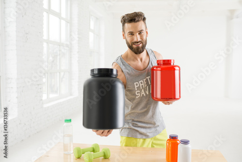 Fotografia Athletic man holding bottles with sports nutriton in the white gym interior