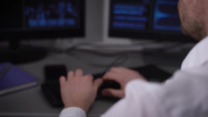 Poster - Back view of a young businessman with smartwatch on his hand working at his desk in the office. Image of hands of a manager sitting in front of computer monitors and typing on keyboard.