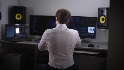 Fototapete - Young software developer analyzes and introduces a large amount of electronic data while working on a new software project. A couple of monitors and a laptop used when working on complex programs.