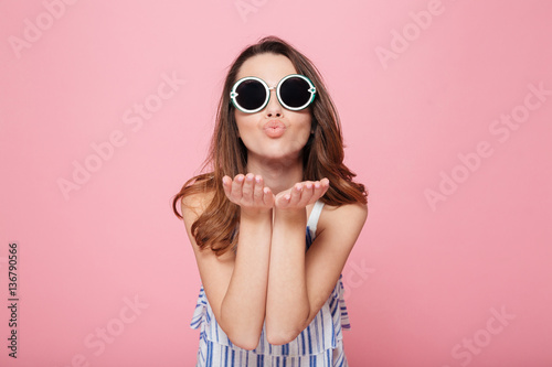 Fotografie, Obraz Cute young woman in round sunglasses standing and sending kiss