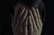 Concept of fear, domestic violence. Woman covers her face her hands. Dim light and black  background , creates a dramatic mood of this  image.
