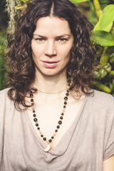 Wall Mural - Beautiful woman with curly brown hair in the exotic green garden