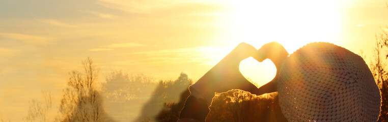  Heart Symbol.  Woman hands in gloves heart symbol shaped, on a beautiful sunset light background.