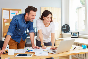 Wall Mural - Happy couple running business together working on laptop at office