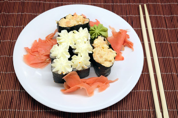 Sushi pieces on white plate and two chopsticks over brown wicker straw mat top view closeup