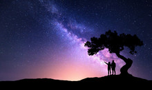 Milky Way With People Under The Tree On The Hill. Landscape With Night Starry Sky And Silhouette Of Standing Happy Man And Woman Who Pointing Finger In Starry Sky. Milky Way With Travelers. Universe