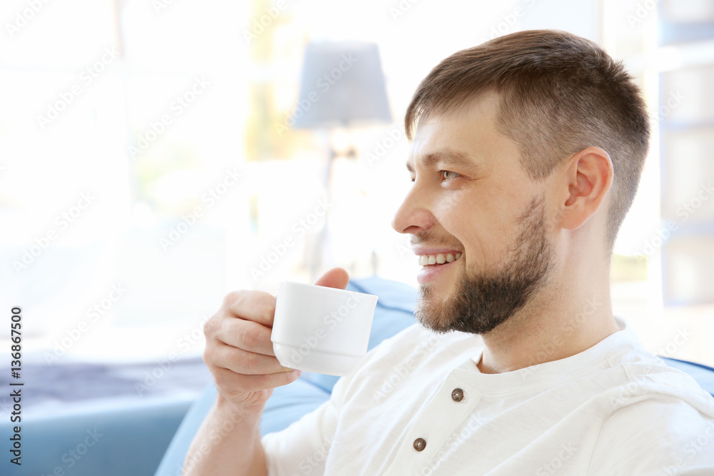 Handsome young man drinking coffee at home, closeup