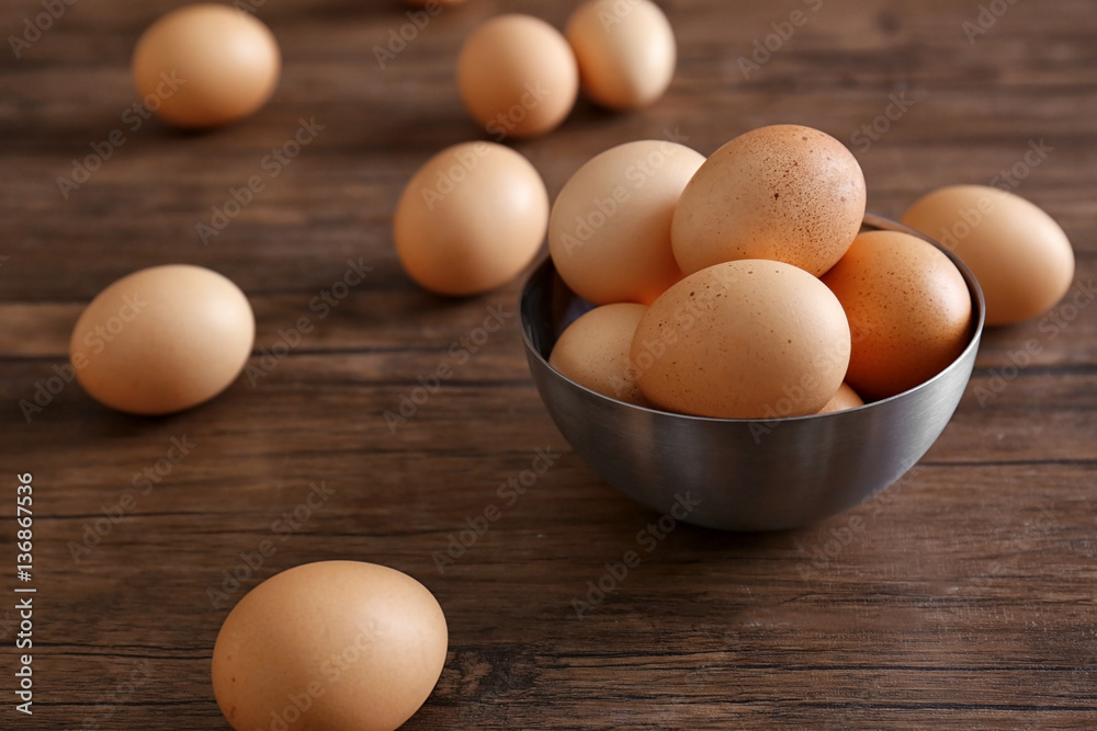 Raw eggs in bowl on wooden background