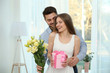 © Africa Studio - Handsome young man giving present and bouquet of flowers to his girlfriend at home