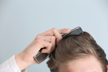 Wall Mural - Handsome young man combing hair on color background, closeup