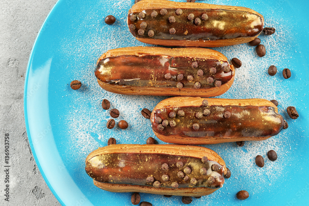 Delicious eclairs on blue plate, top view