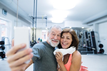 Wall Mural - Senior couple in gym resting, taking selfie with smartphone