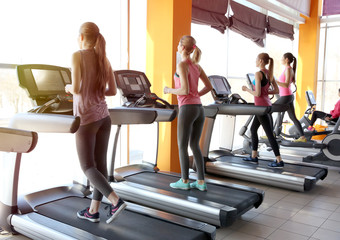 Poster - Young sporty women running on treadmills in gym