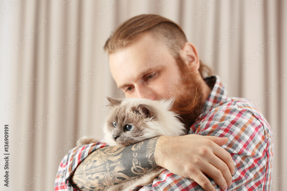 Young bearded man holding fluffy cat on blurred background