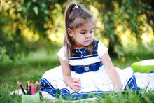Маленькая девочка рисует лежа на траве в парке
