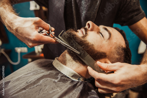 Fotografie, Obraz Professional Master hairdresser cuts client beard.