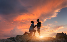 Silhouettes Of A Man Making Marriage Proposal To His Girlfriend On The Mountain Peak At Sunset. Landscape With Silhouette Of Lovers Against Colorful Sky. Couple. People, Relationship. Traveling Couple