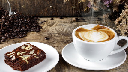 Cappuccino Coffee and sweet chocolate brownies cake. A cup of latte, cappuccino or espresso coffee with milk put on a wood table with dark roasting coffee beans. Drawing the foam milk on top.