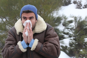man blowing his nose in the cold weather