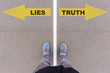 Lies vs truth text arrows on asphalt ground, feet and shoes on f