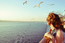 Girl Looking At The Calm Sea On The Sunset With Wind In Her Hair And Seagulls On The Background