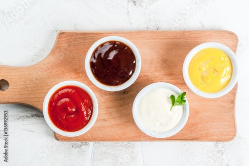 Fotografie, Obraz Classic set of sauces in white saucers: American yellow mustard, ketchup, barbecue sauce, mayonnaise
