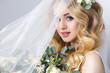 Beauty portrait of a beautiful blonde bride in veil with a bouquet of flowers in his hands on a gray background.