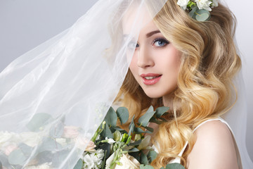 beauty portrait of a beautiful blonde bride in veil with a bouquet of flowers in his hands on a gray