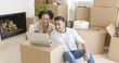 © Dash - Happy mixed race couple sitting on the floor among unpacked carton boxes and using laptop computer to plan the future in their new apartment they just moved in.