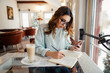 Young business woman in cafe writes notes in notebook from smartphone