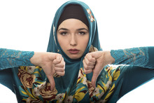 Female Wearing A Hijab, Conservative Fashion For Muslims, Middle East And Eastern European Culture.  She Is Isolated On A White Background And Holding Thumbs Down In Disapproval