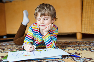 Wall Mural - preschool kid boy at home making homework, painting a story with colorful pens