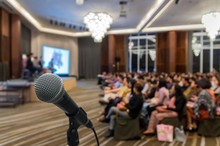 Microphone Over The Abstract Blurred Photo Of Conference Hall Or